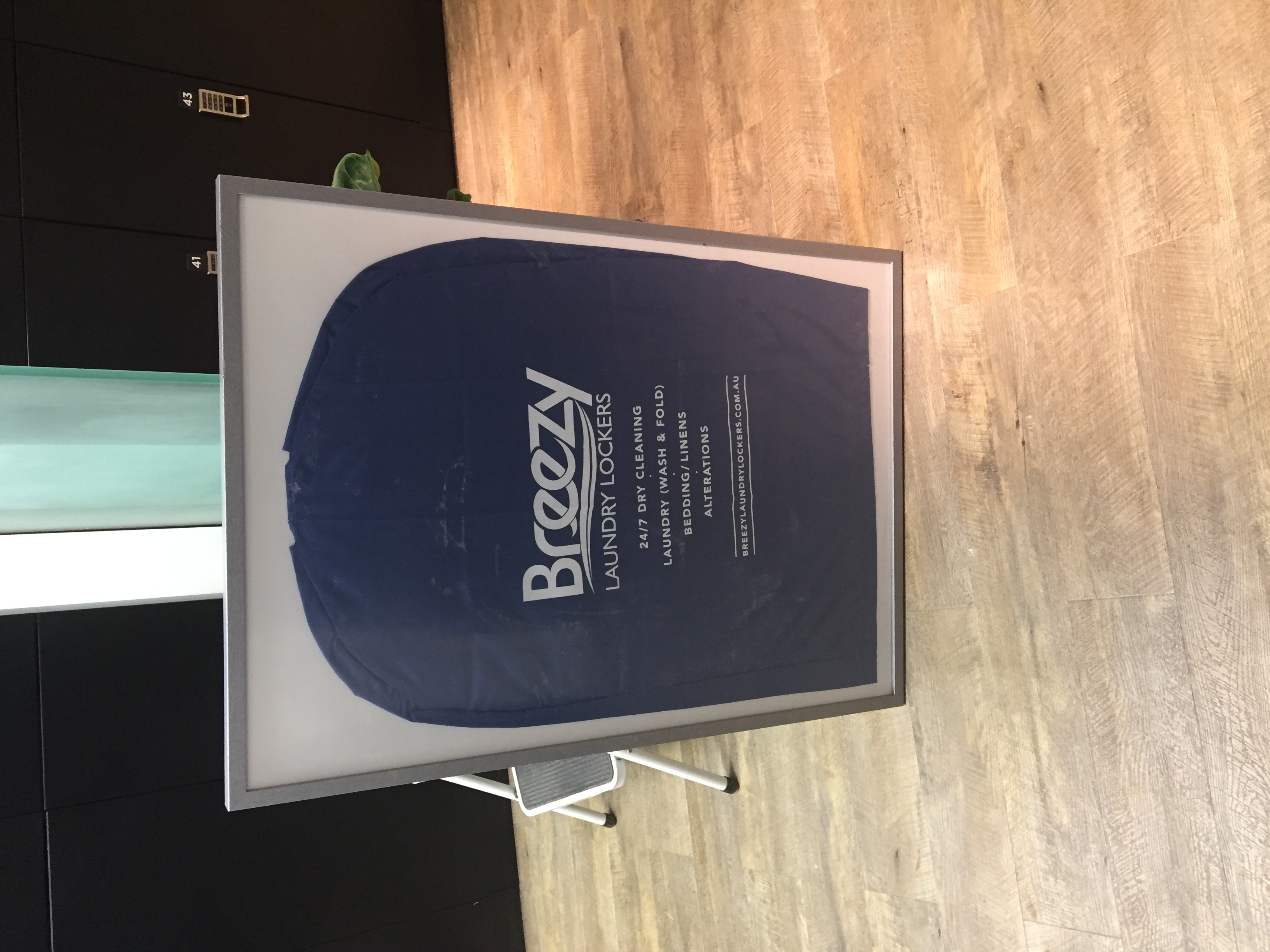 Branded poster on an easel listing the 24/7 services available: dry cleaning, wash and fold, bedding, alterations