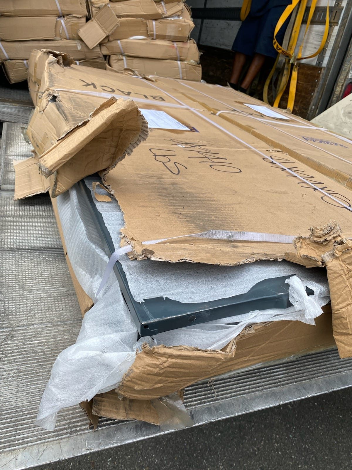 Close up of damaged cardboard packaging showing the bare metal frame of a laundry locker exposed through torn box walls