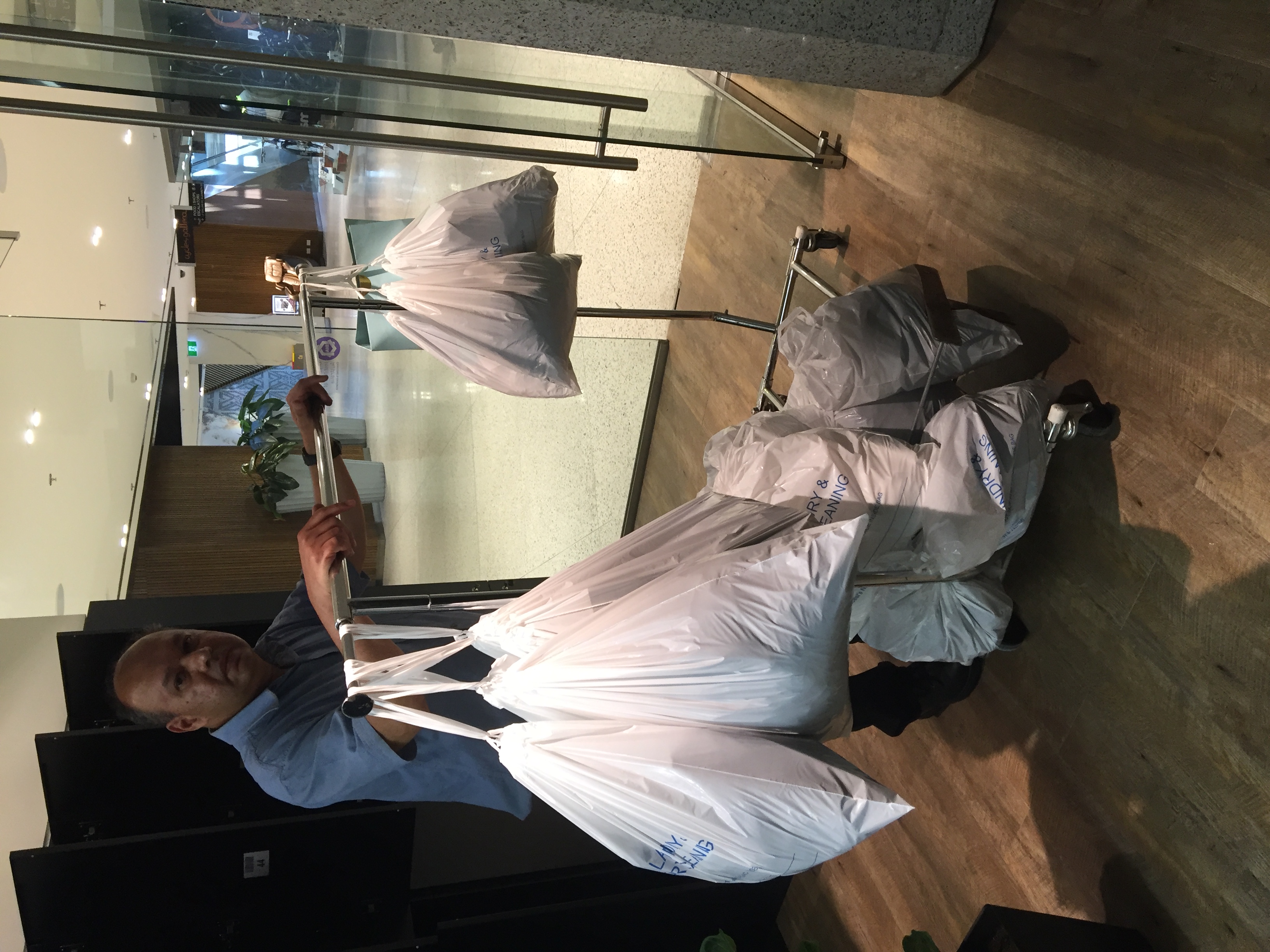 The operator pushing a rack stacked with finished laundry orders in white laundry bags through the mall corridor toward the locker store