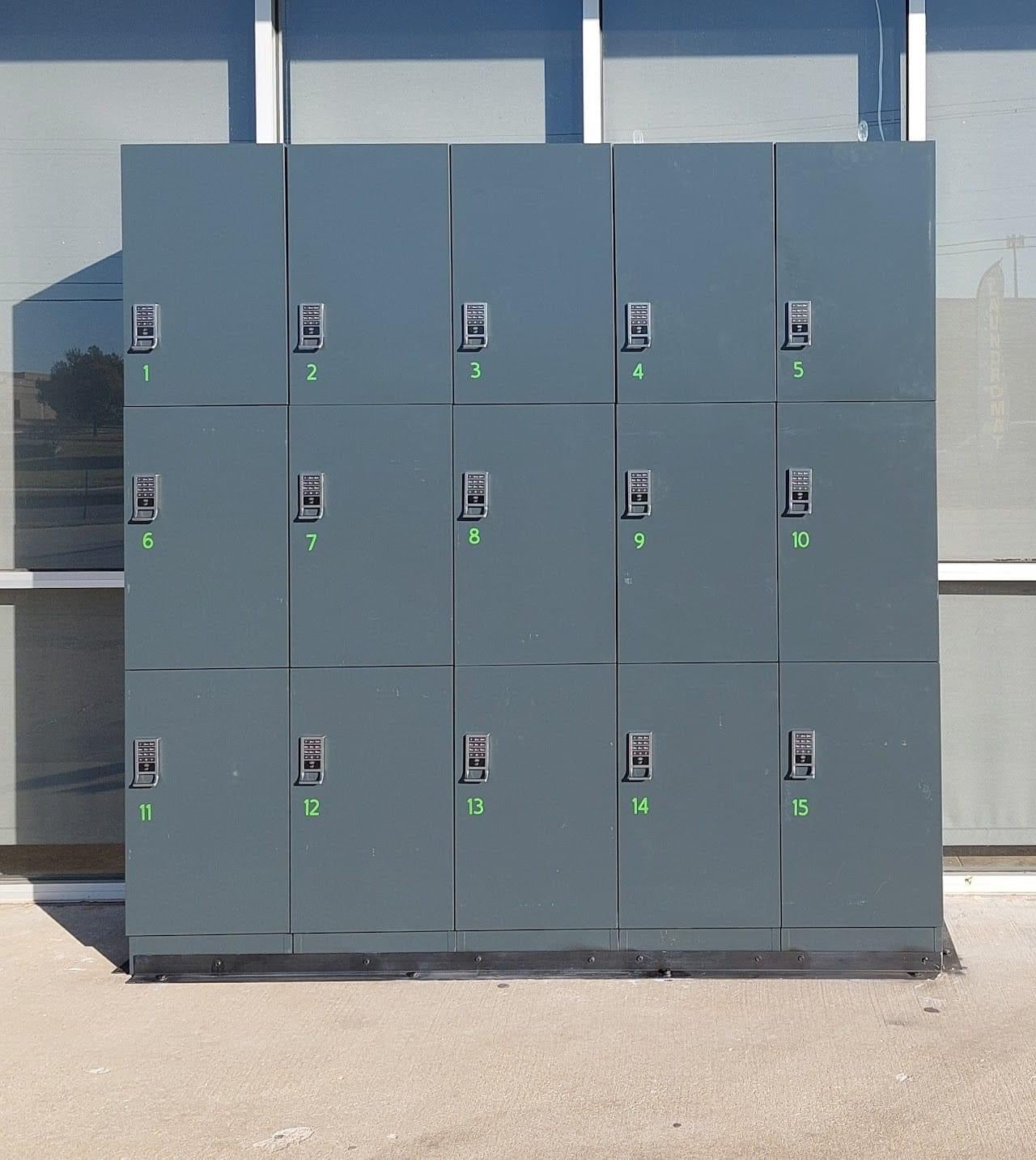 A bank of fifteen grey smart laundry lockers installed at the exterior of a laundromat